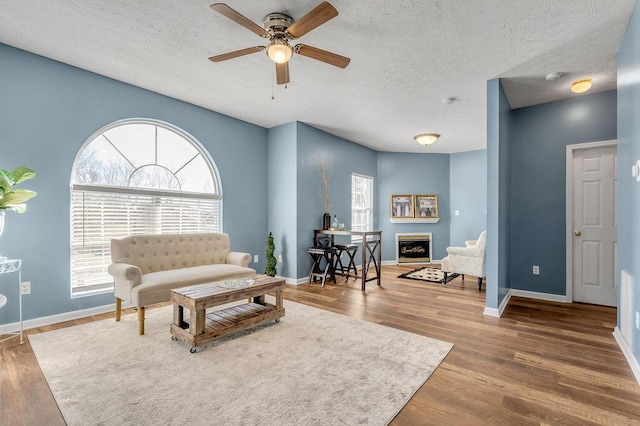 living room featuring a textured ceiling, a fireplace, wood finished floors, and baseboards