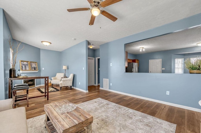 living room with visible vents, baseboards, a ceiling fan, wood finished floors, and a textured ceiling