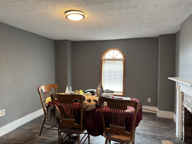 dining room with dark hardwood / wood-style floors, a textured ceiling, and a brick fireplace