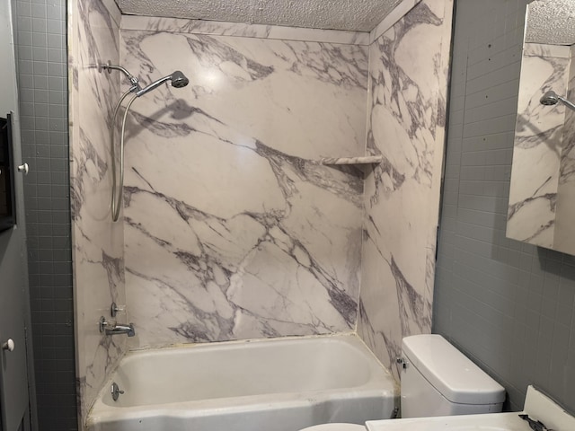 bathroom with toilet, a textured ceiling, and tiled shower / bath