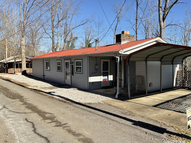 view of front of home with metal roof, a detached carport, and a chimney