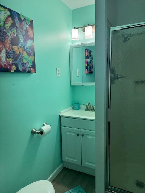 full bath with vanity, wood finished floors, baseboards, a shower stall, and toilet