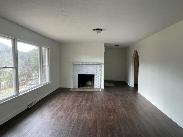 unfurnished living room with dark wood-type flooring and a brick fireplace