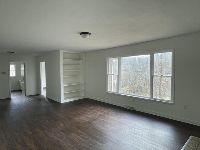 spare room with built in shelves and dark hardwood / wood-style floors