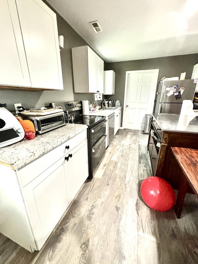 kitchen with light stone countertops, white cabinetry, stainless steel appliances, a textured ceiling, and light wood-type flooring