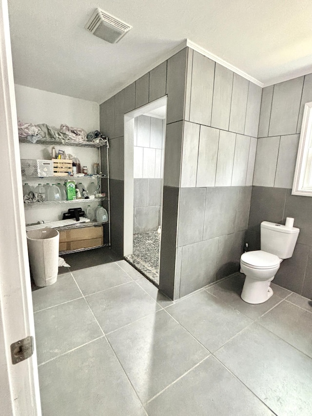 bathroom featuring tile patterned floors, toilet, tile walls, and walk in shower