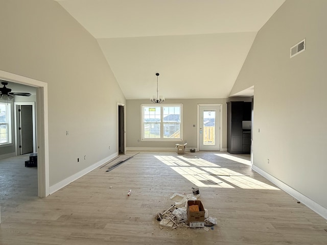 unfurnished dining area with ceiling fan with notable chandelier, light hardwood / wood-style floors, and high vaulted ceiling