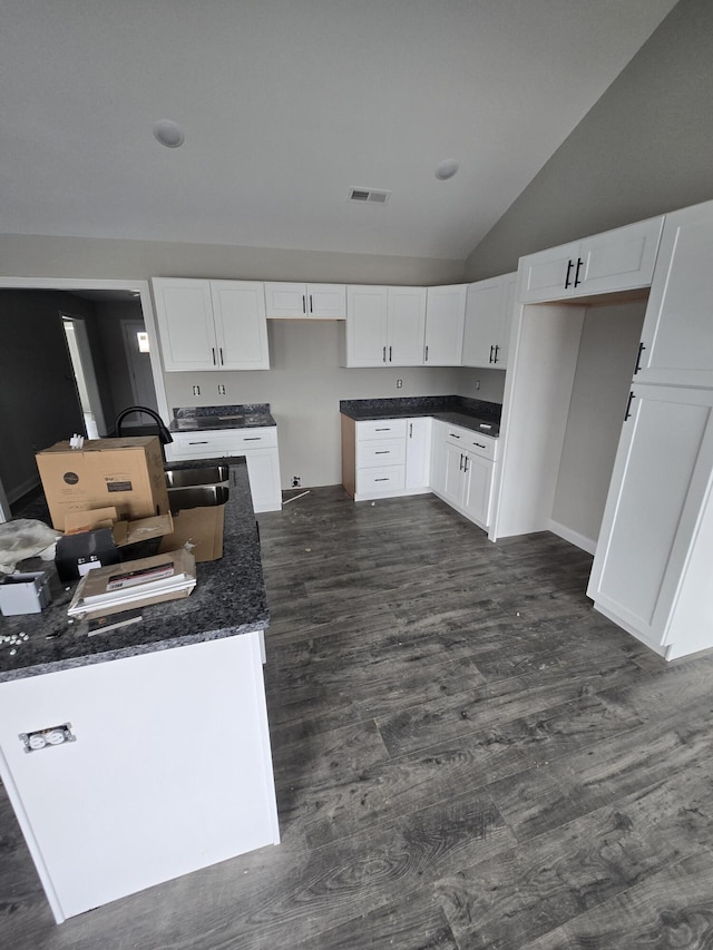 kitchen featuring dark stone countertops, lofted ceiling, sink, dark wood-type flooring, and white cabinets