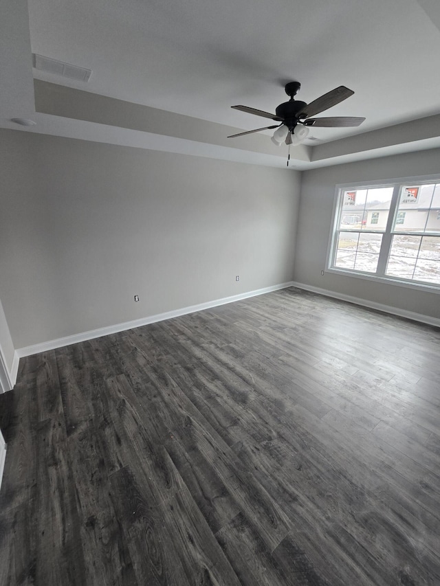 unfurnished room with a tray ceiling, ceiling fan, and dark hardwood / wood-style flooring