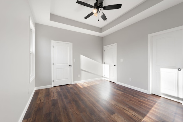 empty room featuring a tray ceiling, ceiling fan, and dark wood-type flooring