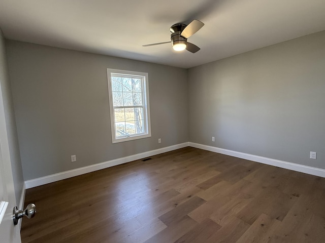 spare room featuring dark wood-style floors, ceiling fan, visible vents, and baseboards