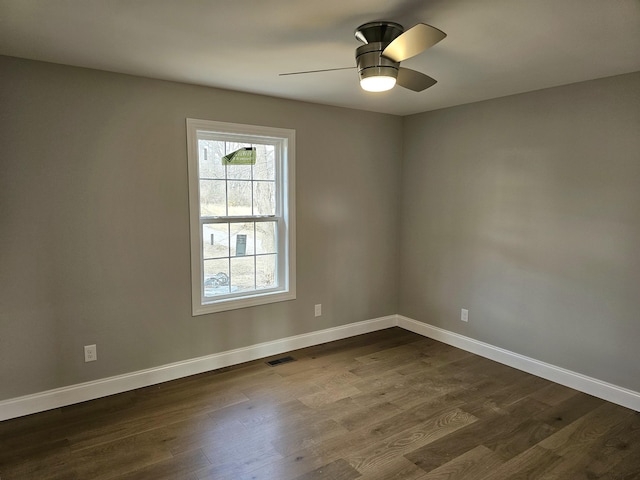 spare room with a ceiling fan, visible vents, dark wood finished floors, and baseboards