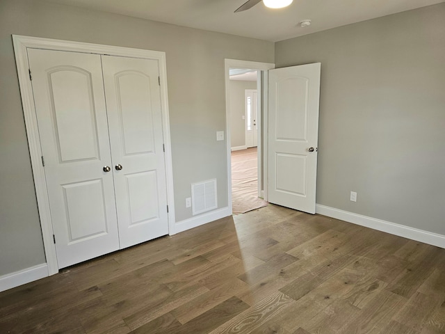 unfurnished bedroom with a closet, visible vents, a ceiling fan, wood finished floors, and baseboards