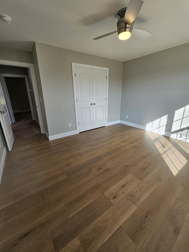 unfurnished bedroom with a closet, dark wood finished floors, a ceiling fan, and baseboards