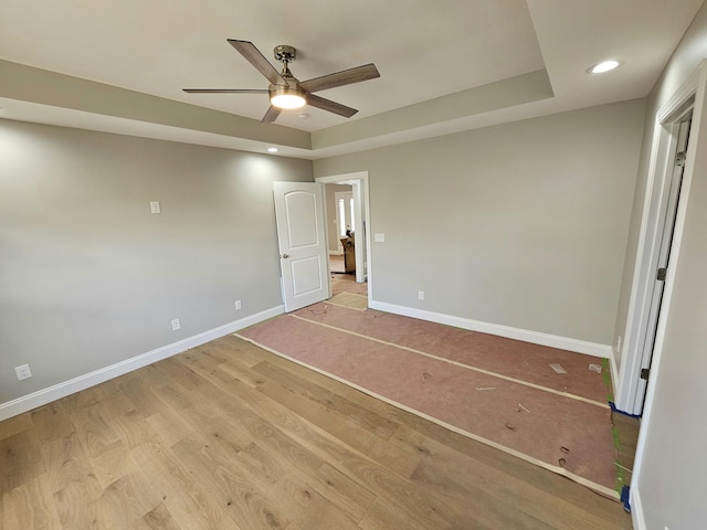 unfurnished bedroom with baseboards, a ceiling fan, light wood-style flooring, a tray ceiling, and recessed lighting