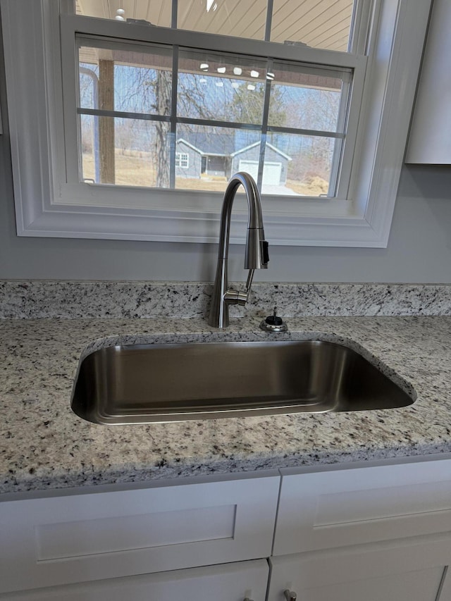 details featuring light stone counters, white cabinets, and a sink