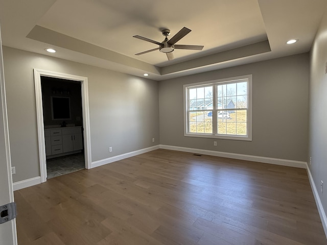 unfurnished bedroom with a tray ceiling, wood finished floors, and baseboards