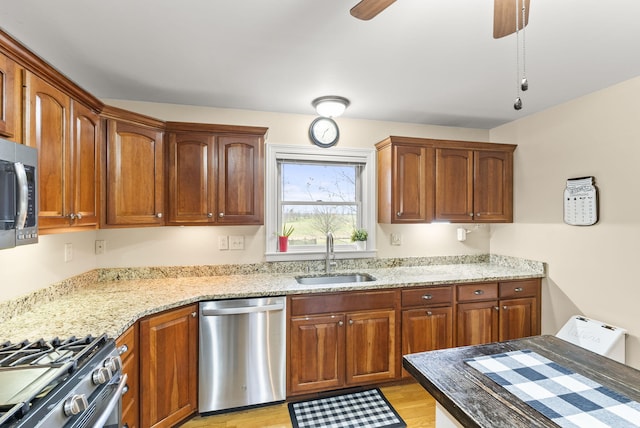 kitchen with ceiling fan, sink, light stone counters, light hardwood / wood-style flooring, and appliances with stainless steel finishes