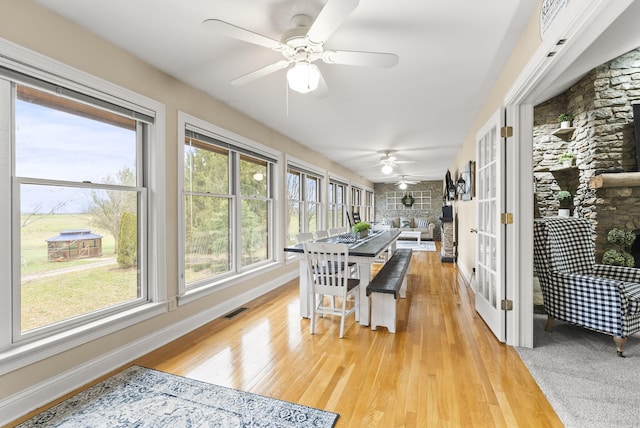 sunroom with a stone fireplace and ceiling fan