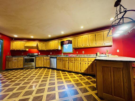 kitchen with kitchen peninsula, appliances with stainless steel finishes, premium range hood, sink, and hanging light fixtures