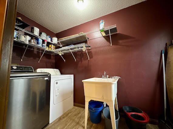 laundry room with light hardwood / wood-style floors, a textured ceiling, and washing machine and clothes dryer