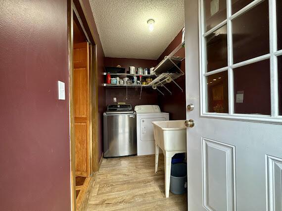 laundry room with independent washer and dryer, a textured ceiling, and light hardwood / wood-style flooring