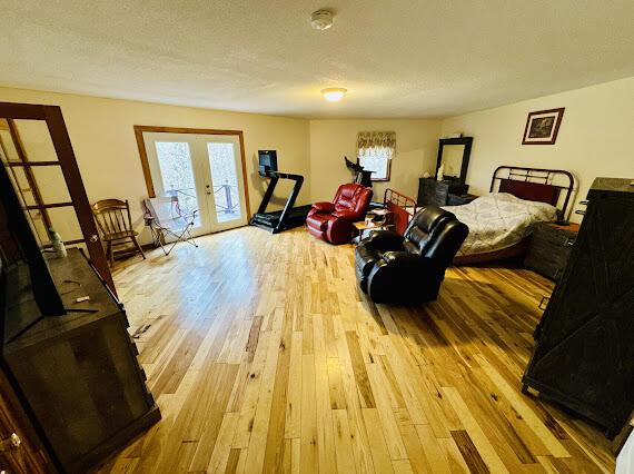 bedroom featuring light hardwood / wood-style floors, access to exterior, a textured ceiling, and french doors