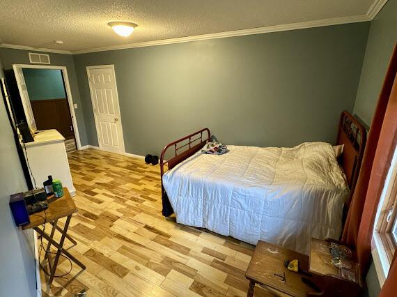 bedroom featuring a textured ceiling, light hardwood / wood-style floors, and crown molding