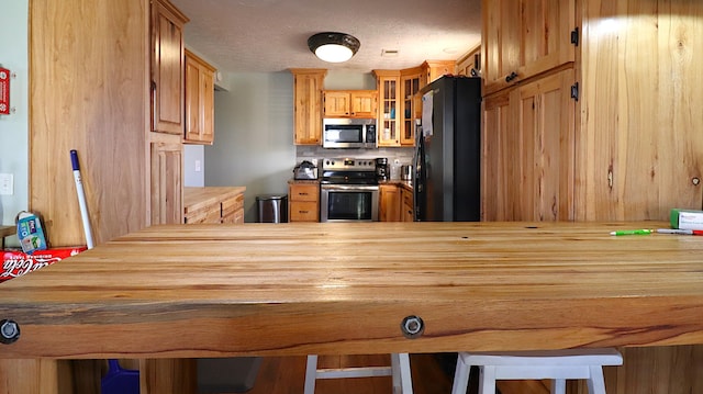 kitchen featuring kitchen peninsula, appliances with stainless steel finishes, backsplash, a kitchen breakfast bar, and a textured ceiling