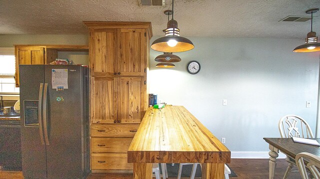 kitchen featuring black fridge, dark hardwood / wood-style flooring, hanging light fixtures, a textured ceiling, and butcher block counters