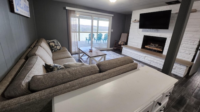 living room with a stone fireplace, dark wood-type flooring, and wooden walls