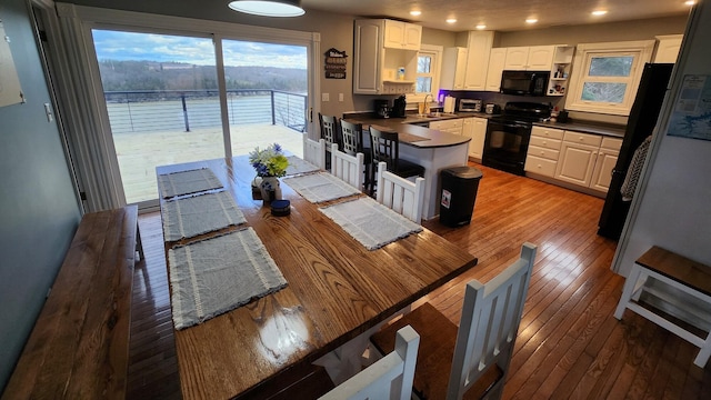 kitchen with sink, hardwood / wood-style flooring, white cabinetry, and black appliances