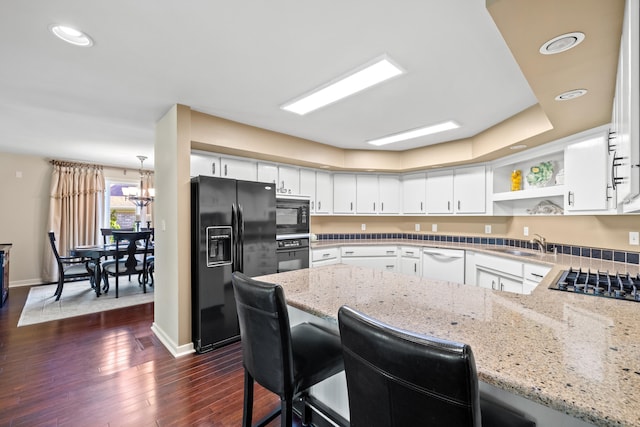 kitchen with light stone countertops, kitchen peninsula, white cabinetry, and black appliances