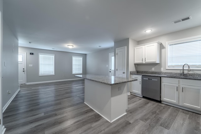 kitchen with a center island, sink, light stone counters, stainless steel dishwasher, and white cabinets