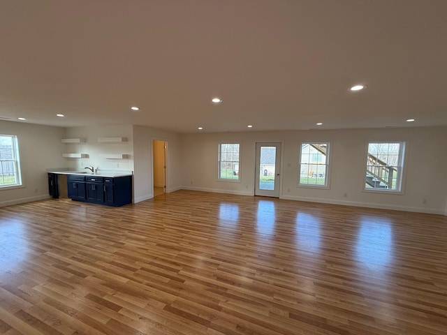 unfurnished living room with light hardwood / wood-style flooring, sink, and a wealth of natural light