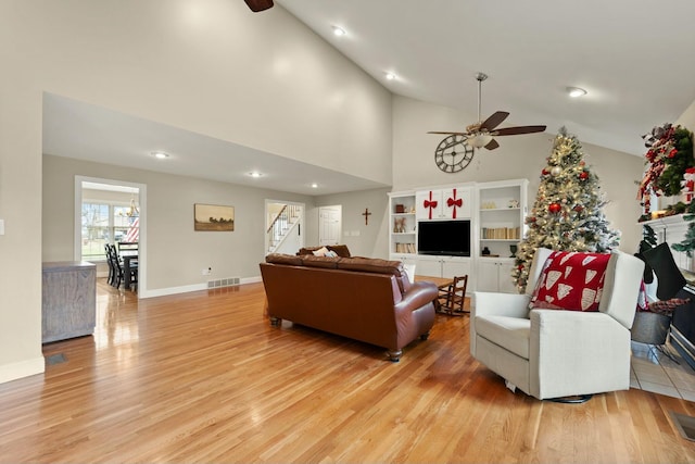 living room with built in shelves, ceiling fan, high vaulted ceiling, and light wood-type flooring