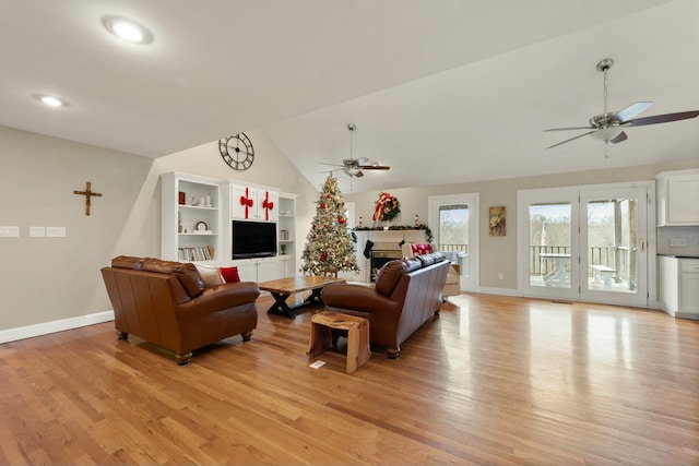 living room featuring built in features, light hardwood / wood-style floors, vaulted ceiling, and ceiling fan