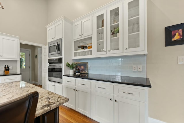 kitchen with white cabinetry, stainless steel microwave, oven, and dark stone counters