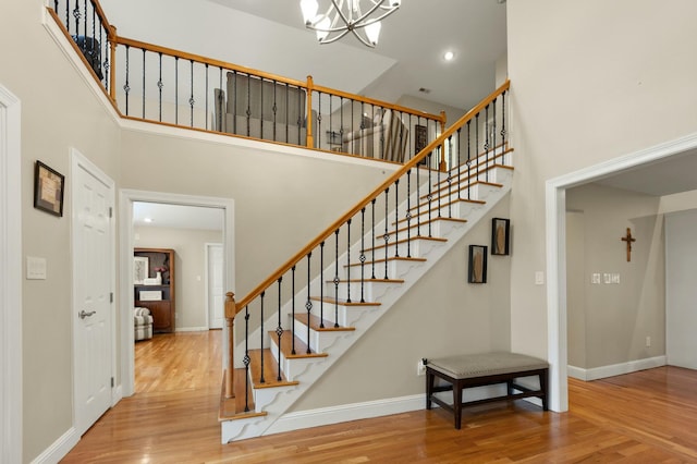 stairs featuring a chandelier, wood-type flooring, and a high ceiling