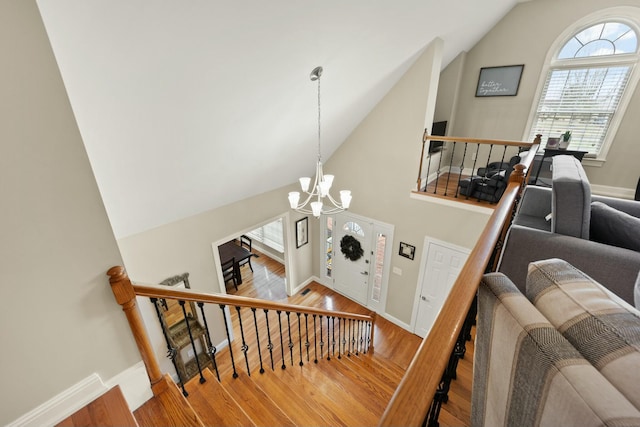 stairway featuring hardwood / wood-style flooring, a healthy amount of sunlight, lofted ceiling, and an inviting chandelier