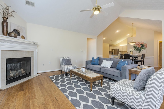 living room featuring hardwood / wood-style floors, ceiling fan, vaulted ceiling, and a tiled fireplace