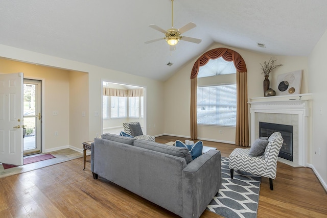 living room with a tile fireplace, light wood-type flooring, ceiling fan, and lofted ceiling