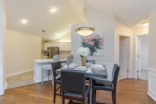 dining area with a textured ceiling, light wood-type flooring, sink, and vaulted ceiling