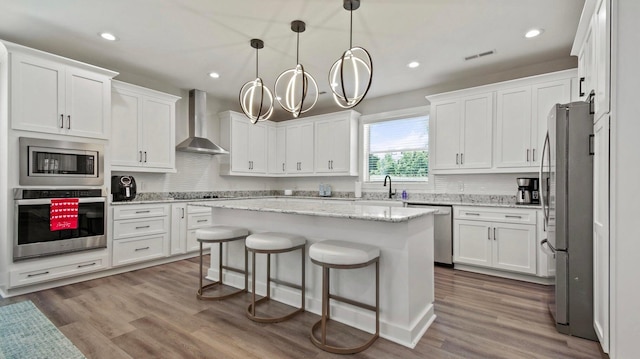 kitchen featuring appliances with stainless steel finishes, white cabinetry, and wall chimney range hood