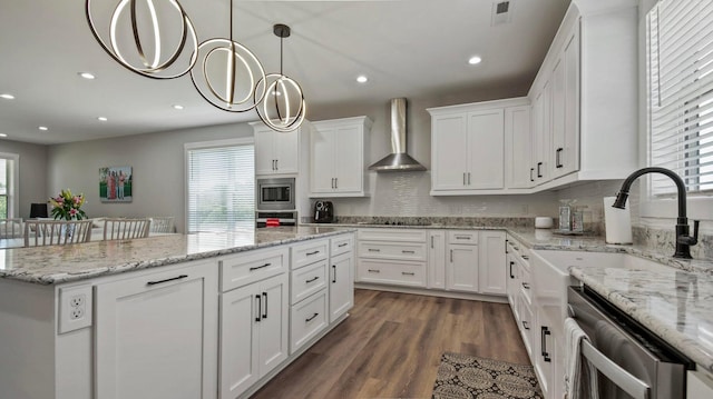 kitchen with wall chimney exhaust hood, dark wood-type flooring, hanging light fixtures, white cabinets, and appliances with stainless steel finishes