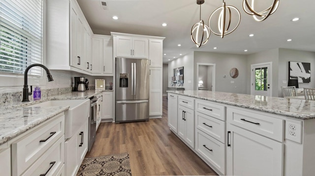 kitchen with light stone counters, stainless steel appliances, a chandelier, white cabinetry, and hanging light fixtures