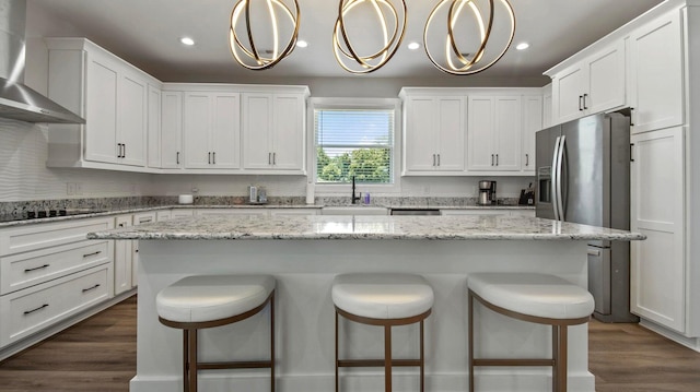 kitchen featuring white cabinets, wall chimney exhaust hood, a center island, and hanging light fixtures