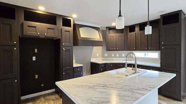 kitchen featuring sink, an island with sink, hanging light fixtures, and light wood-type flooring