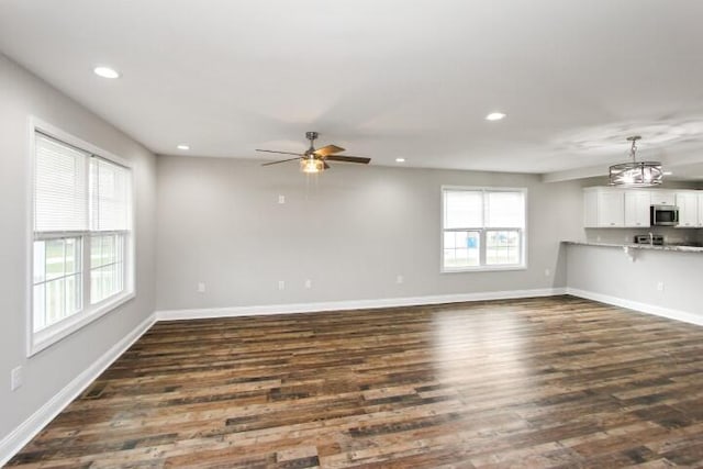 unfurnished living room with dark hardwood / wood-style flooring, ceiling fan, and a healthy amount of sunlight