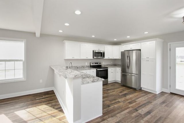 kitchen with kitchen peninsula, appliances with stainless steel finishes, light stone countertops, dark hardwood / wood-style floors, and white cabinetry